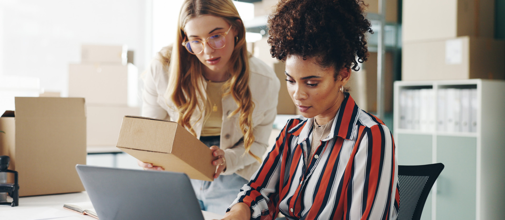Two women working together with a laptop and packages in an office